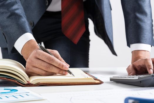 Close-up businessman hand writing to do list in diary at desk. Financial expertise and consulting. Manager in suit and tie planning day with personal organizer. Time management and work organization.
