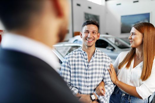 Man car salesman telling about the features of the new car to the couple at dealership