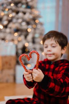 A boy in pajamas with caramel under the Christmas tree . New Year's candies are red. New Year's mood.