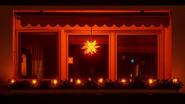 Bright shining X-Mas star in a window of a night. Traditional decor of the Christmas season with the view over an illuminated balcony