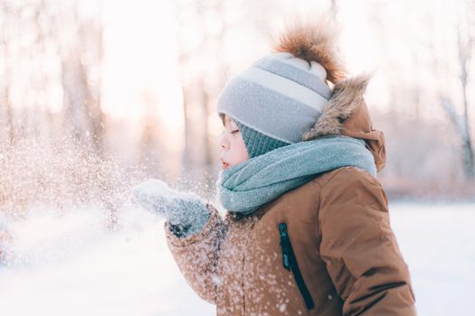 A boy blows snow off his hands winter lifestyle . Winter painting. Snow Park. Cold. Happy childhood