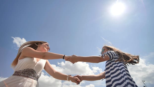 Happy girlfriends are spinning by the arms on a warm summer day