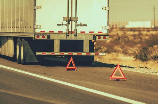 Heavy Transportation Theme. Broken Semi Truck on Side of a Highway Trailer Close Up and Warning Triangles. Roadside Asssitance.