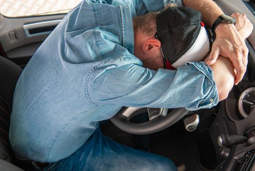 Tired Exhausted Truck Driver Sleeping on the Vehicle Steering Wheel Inside Truck Cabin. 