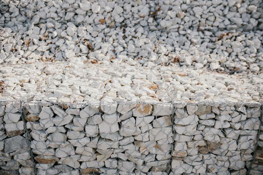 strengthening the slope with stones behind the wire. grey texture. construction. Granite stones behind a metal grate