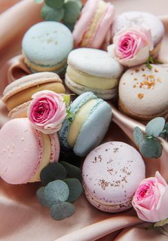 Beautiful colorful tasty macaroons, roses and eucalyptus on a textile background