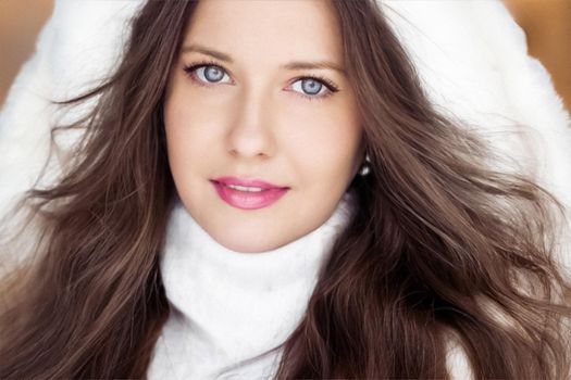 Winter fashion and Christmas holiday look. Beautiful woman wearing white sweater and fluffy fur coat with hood wrap, glamour makeup and hairstyle as xmas portrait.