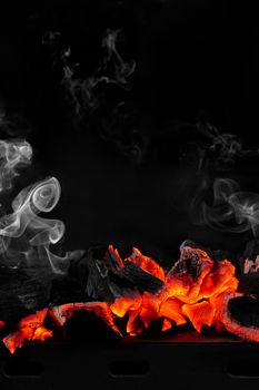 Red hot smouldering charcoals on metal tray of bbq grill on black background with light white smoke. Vertical image