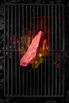 Top view of piece of veal tenderloin cooking on black cast iron grill grate over burning charcoals. Barbecue or cookout menu concept