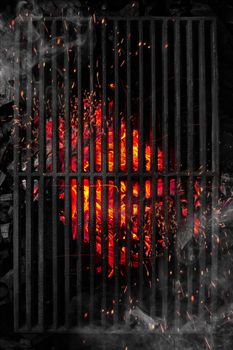 Top view through black metal barbecue grate of burning coals with soaring bright sparks and light white smoke