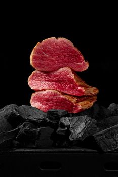 Pieces of juicy, lightly seared veal tenderloin on charcoal on black background. Barbecue menu concept