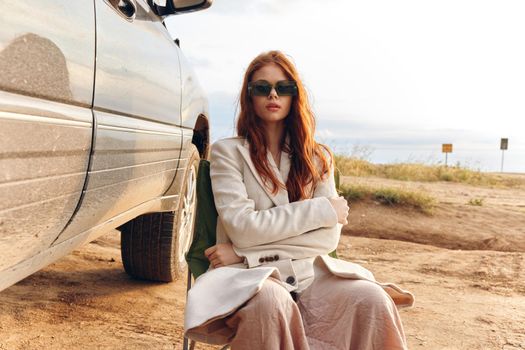 pretty woman in a coat outdoors sitting on a chair near the car endless field. High quality photo