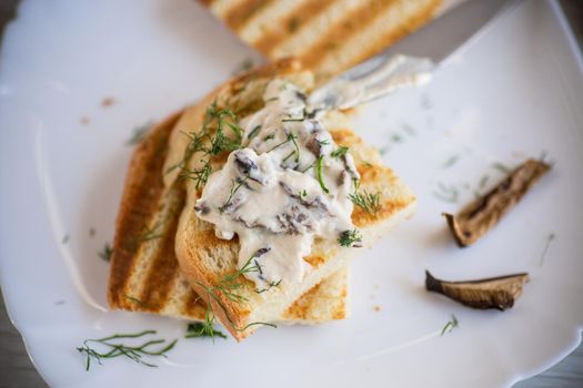 fried bread toast with cheese spread with boiled dried mushrooms, in a plate on a wooden table.