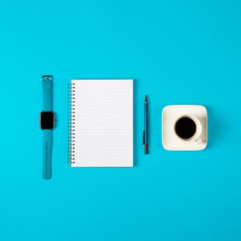 Notepad, watch, pen and a cup of coffee isolated on blue background. Notepad with copy space. Office, business, discreet style.