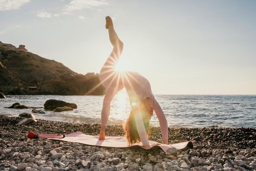 Young woman with black hair, fitness instructor in pink sports leggings and tops, doing pilates on yoga mat with magic pilates ring by the sea on the beach. Female fitness daily yoga concept