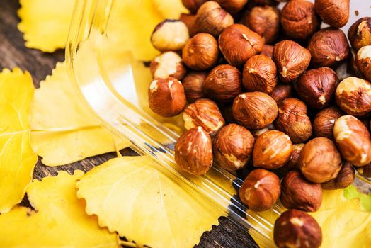 Raw Organic Hazelnuts in the Clear Plastic Box on Wooden Planks with Yellow Leaves. 