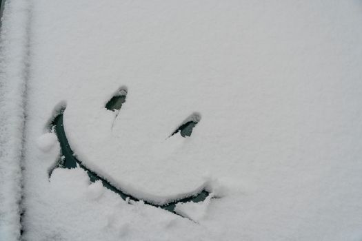 Snow background. Texture of wet snow with a cheerful smiley symbol pattern in the winter window of the car outdoors close-up. Smile in the snow, happy cheerful image. Winter time concept