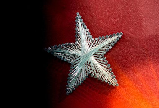 A star made from steel nails and string on a red background