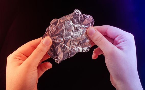 Hand tearing a heart shaped aluminium foil on a wooden background
