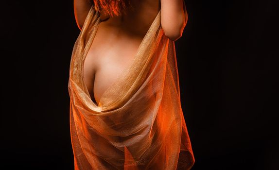 Young nude woman posing in studio with a golden shawl on a dark background. View from the back. 