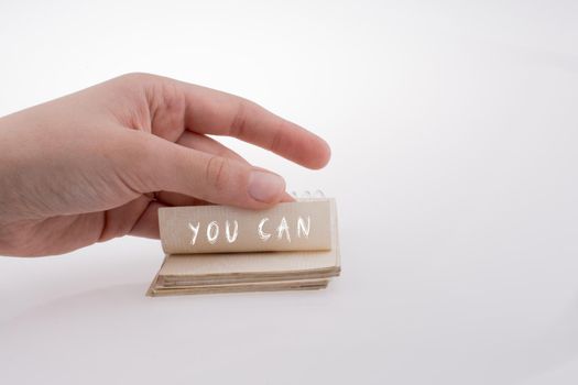 Hand holding paper with note YOU CAN on a white background