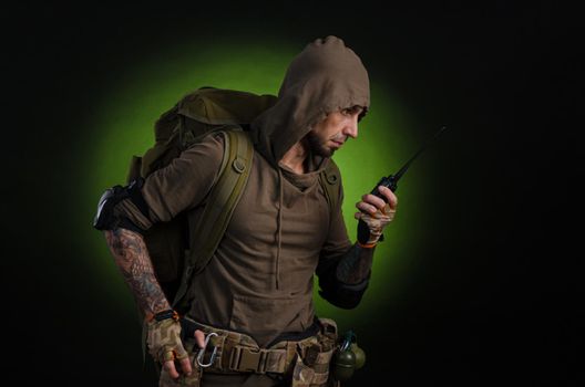 man Stalker with a gun with an optical sight and a backpack on a dark background with emotions looking, aiming, watching, sneaking