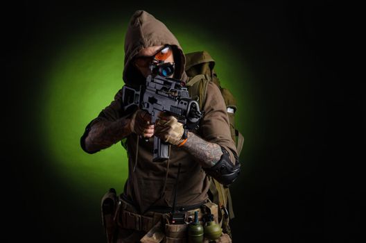 man Stalker with a gun with a telescopic sight and a backpack in a gas mask on a dark background with emotions looking, aiming, watching, sneaking