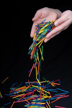 Hand letting coloured wooden  sticks fall on black background