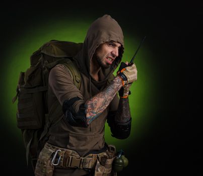 man Stalker with a gun with an optical sight and a backpack on a dark background with emotions looking, aiming, watching, sneaking