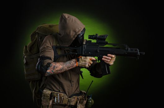 man Stalker with a gun with a telescopic sight and a backpack in a gas mask on a dark background with emotions looking, aiming, watching, sneaking