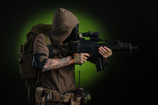 man Stalker with a gun with a telescopic sight and a backpack in a gas mask on a dark background with emotions looking, aiming, watching, sneaking