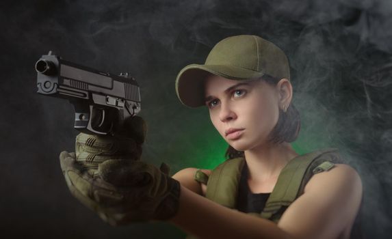 girl in military special clothes posing with a gun in his hands on a dark background in the haze