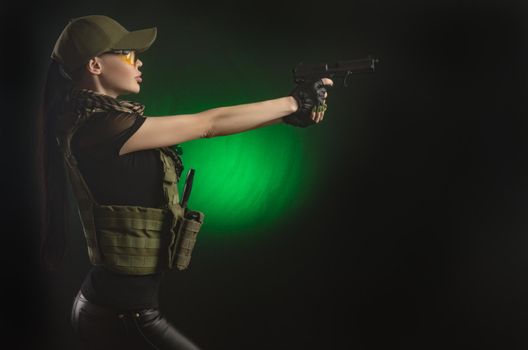 girl in military special clothes posing with a gun in his hands on a dark background in the haze