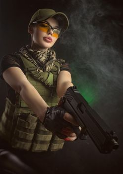 girl in military special clothes posing with a gun in his hands on a dark background in the haze