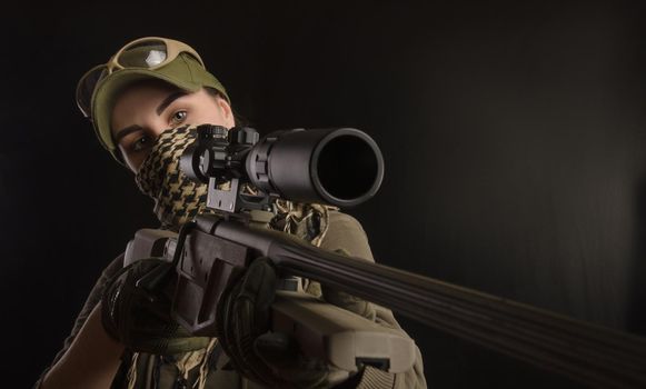 girl in military special clothes posing with a gun in his hands on a dark background in the haze