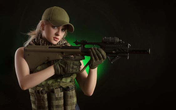 girl in military special clothes posing with a gun in his hands on a dark background in the haze