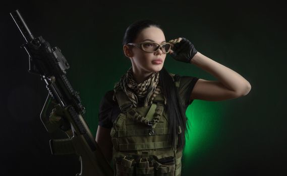 girl in military special clothes posing with a gun in his hands on a dark background in the haze