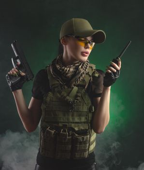 girl in military special clothes posing with a gun in his hands on a dark background in the haze