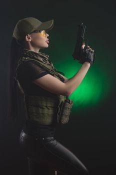 girl in military special clothes posing with a gun in his hands on a dark background in the haze