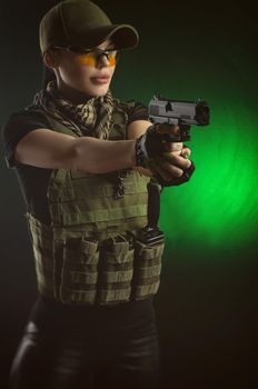 girl in military special clothes posing with a gun in his hands on a dark background in the haze