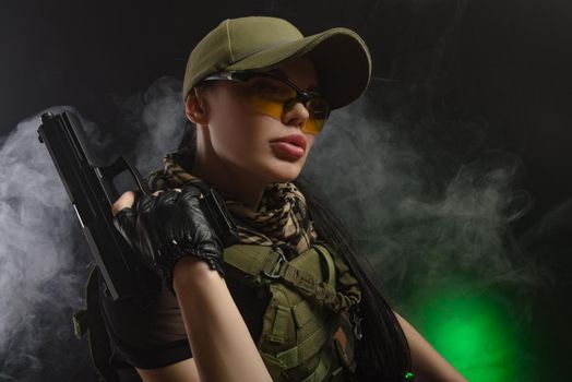 girl in military special clothes posing with a gun in his hands on a dark background in the haze