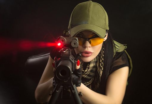 girl in military special clothes posing with a gun in his hands on a dark background in the haze