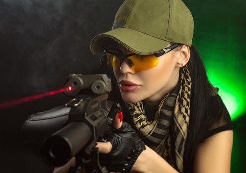 girl in military special clothes posing with a gun in his hands on a dark background in the haze