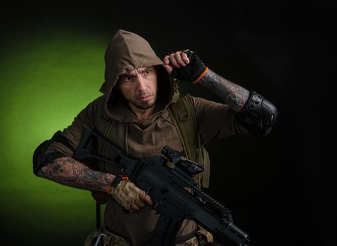 man Stalker with a gun with an optical sight and a backpack on a dark background with emotions looking, aiming, watching, sneaking