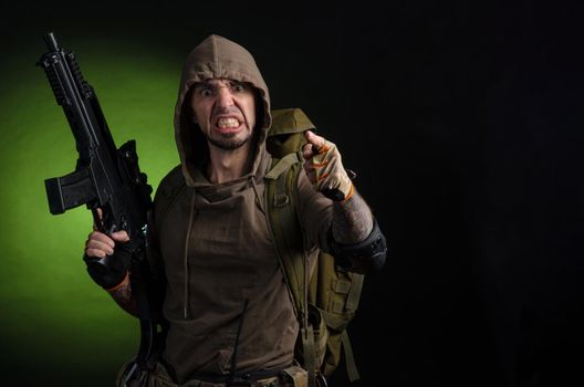 man Stalker with a gun with an optical sight and a backpack on a dark background with emotions looking, aiming, watching, sneaking