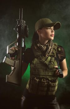 girl in military special clothes posing with a gun in his hands on a dark background in the haze