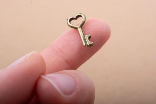 Tiny key with heart shape placed on the finger tip