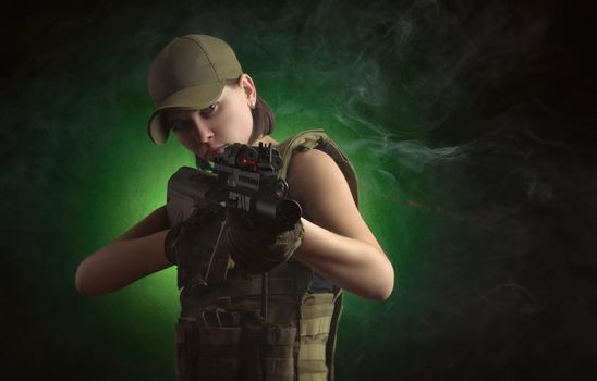 girl in military special clothes posing with a gun in his hands on a dark background in the haze