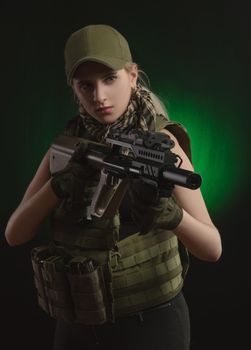 girl in military special clothes posing with a gun in his hands on a dark background in the haze