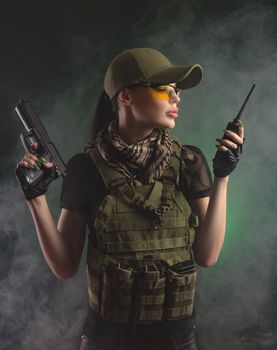 girl in military special clothes posing with a gun in his hands on a dark background in the haze